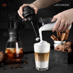 Semi-automatic frother creating rich foam for coffee, with a glass and cookies in the background